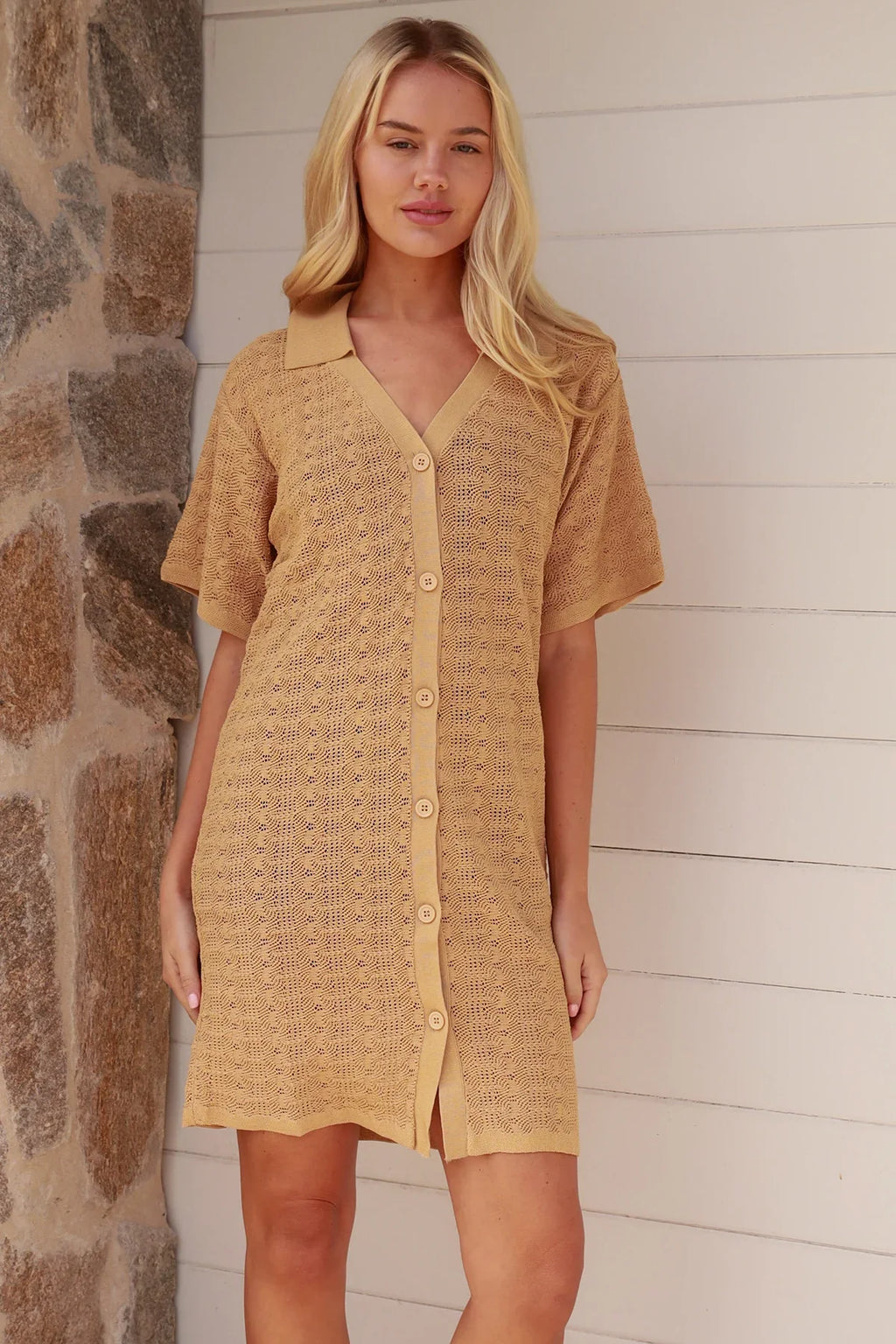Woman wearing a yellow textured dress standing against a stone wall.